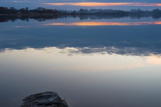 Gray evening sunset above the lake or river. Blue clouds on horizon