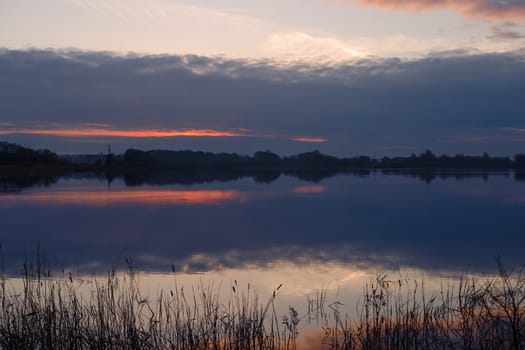 Red evening sunset above the lake or river. Purple and blue clouds and falling sun