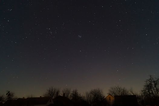 A lond exposure low light photo of village and  night sky. Village far away from city, on sky a lot of stars and constellations. Stock photo of deep sky.