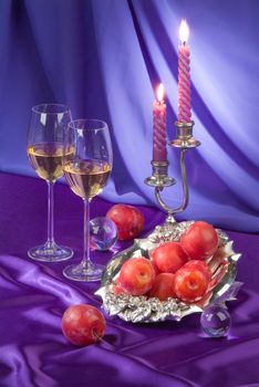 Two glasses, apricots and candles on a fabric studio background