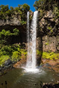 Basalt rock wall, partially covered in lush green rainforest vegetation, behind a curtain of water falling from Chania Waterfall, Aberdares, Kenya, Africa. Looks like its raining. Copy space.