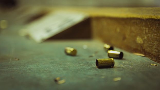 Empty pistol bullet shells on wooden table in a shooting range. Extreme close up and selective focus with blur background.