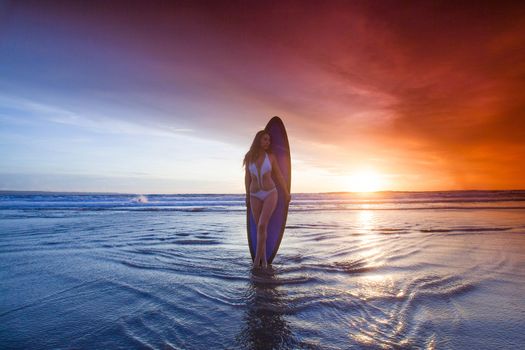 Beautiful surfer woman on the beach at sunset