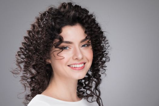 Studio portrait of beautiful smiling woman with curly dark hair on gray background