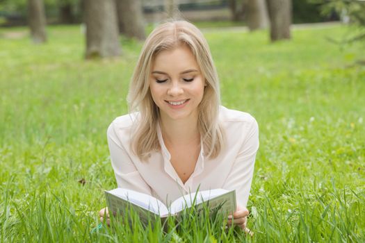 Pretty girl laying on the grass and reading a book in spring park and smiling