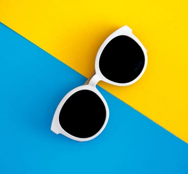 Sunny stylish white sunglasses on a bright blue-cyan and yellow-orange background, top view, isolated. Copy space. Flat lay.