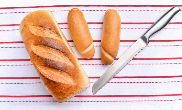 Freshly baked crisp bread on white red striped kitchen towel. Slicing knife with fresh rolls.