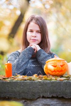 Beautiful teenager girl in autumn garden with halloween pumpkin and candles