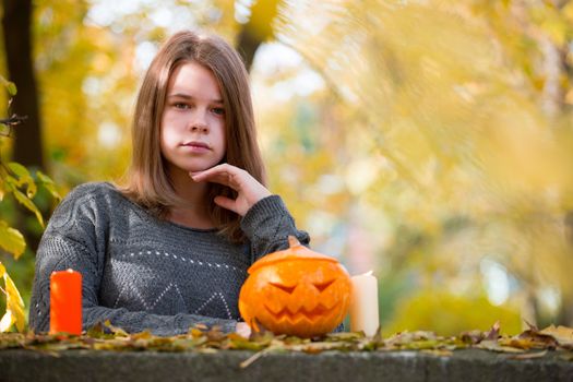 Beautiful teenager girl in autumn garden with halloween pumpkin and candles