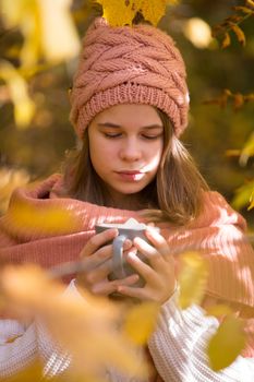 Portrait of pretty nice teenage girl drinking hot cocoa with marshmallows in autumn park