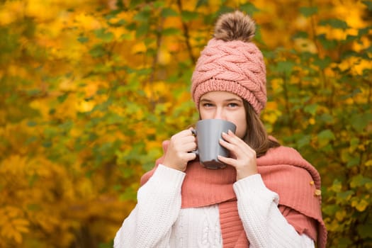 Portrait of pretty nice teenage girl drinking hot cocoa with marshmallows in autumn park