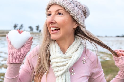 Exuberant happy woman holding a heart of snow in her hand