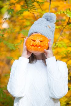 Teenage girl holding halloween pumpkin over orange autumn park background