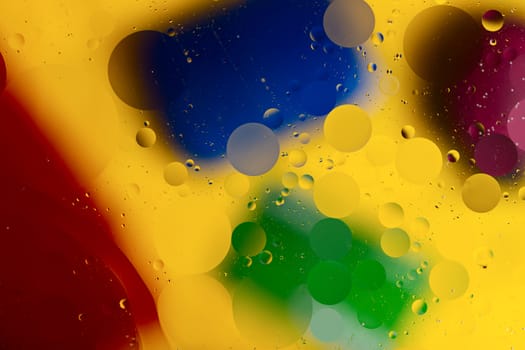 Abstract oil spots in motion on water on blurred yellow background. Red, green, purplee and blue spots on blurred background. Photo with small depth of field.