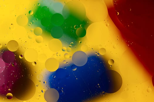 Abstract oil spots in motion on water on blurred yellow background. Red, green, purplee and blue spots on blurred background. Photo with small depth of field.