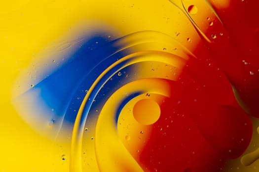 Abstract oil spots in motion on water on blurred yellow background. Red and blue spots on blurred background. Photo with small depth of field.