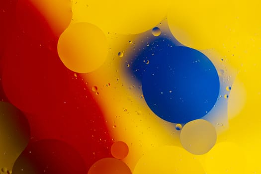 Abstract oil spots in motion on water on blurred yellow background. Red and blue spots on blurred background. Photo with small depth of field.