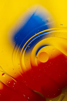Abstract oil spots in motion on water on blurred yellow background. Red and blue spots on blurred background. Photo with small depth of field.