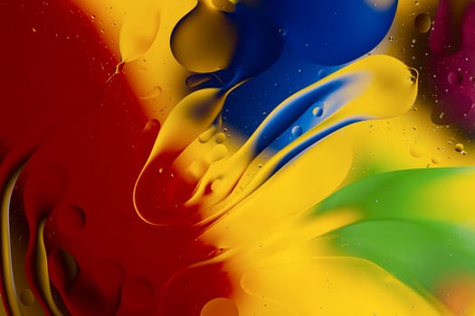 Abstract oil spots in motion on water on blurred yellow background. Red, green, purplee and blue spots on blurred background. Photo with small depth of field.