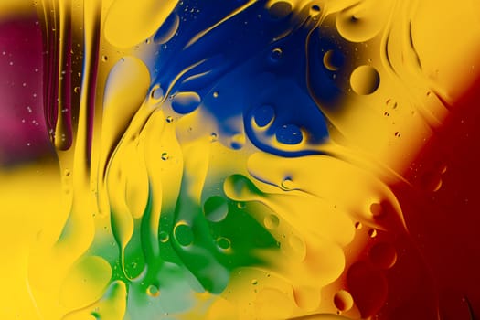 Abstract oil spots in motion on water on blurred yellow background. Red, green, purplee and blue spots on blurred background. Photo with small depth of field.