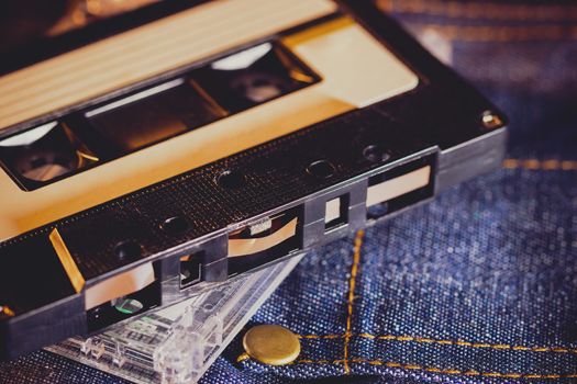 Cassette tape on jeans fabric in darkness. Concept of vintage 90s music player.