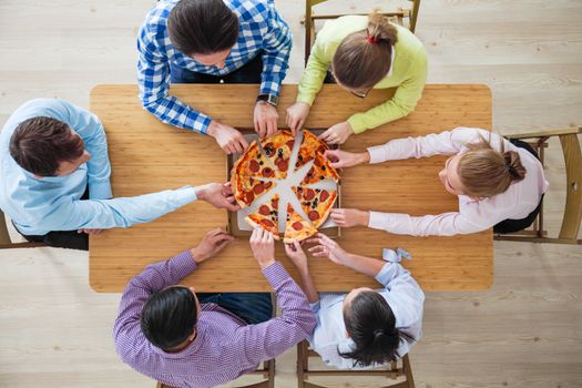 People taking pizza slices from wooden table, top view