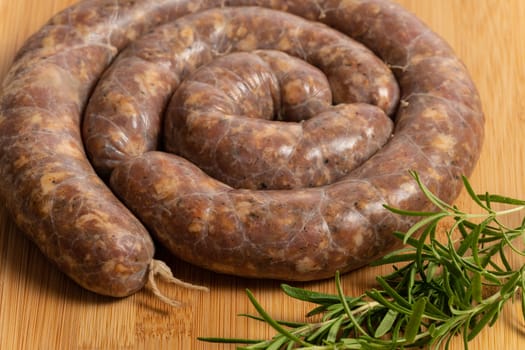 Raw homemade stuffed pork sausages and rosmarin isolated on a wood board.