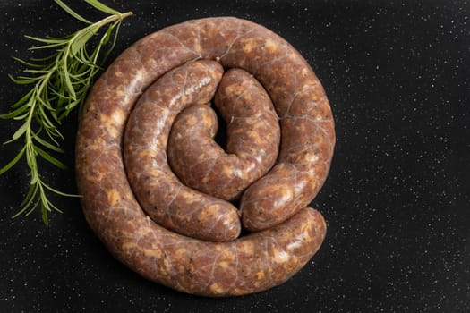Raw homemade stuffed pork sausages and rosmarin isolated on a black background.
