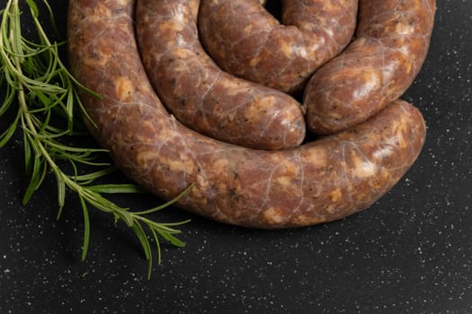 Raw homemade stuffed pork sausages and rosmarin isolated on a black background.