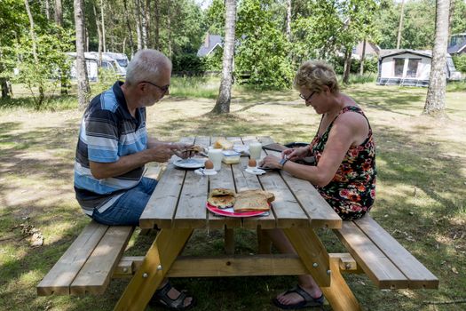 Garderen,Holland,25-june-2019:Couple having lunch at wooden table on the camping in Garderen,garderen is famous because it in the middle of Hooge veluwe national park