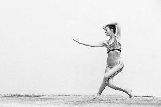 Fit sporty active girl in fashion sportswear doing yoga fitness exercise in front of gray wall, outdoor sports, urban style. Black and white image.