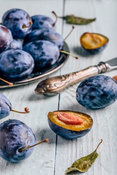 Ripe plums with sliced fruits, leaves and vintage knife over light wooden surface