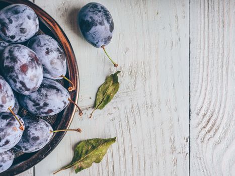 Ripe plums on metal plate over light wooden surface. Copy space