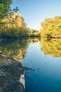 Autumn forest with reflection on water surface of blue lake