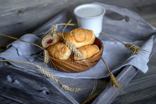 Croissants, a cup with kefir and ears of grain on a wooden tray. The concept of a wholesome breakfast