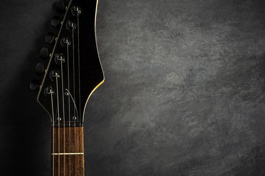 Headstock of black electric guitar on black cement floor. Top view and copy space for text. Concept of rock music.