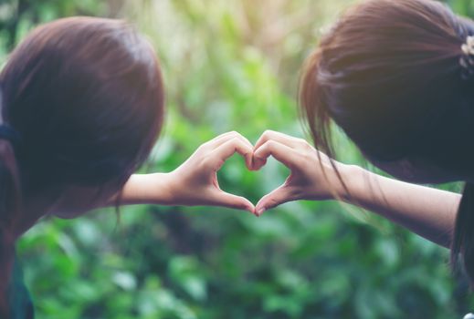 women making heart shapes with their hands on nature green background