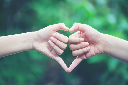 women making heart shapes with their hands on nature green background