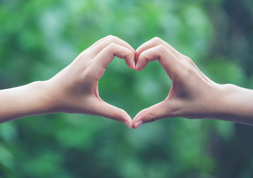 women making heart shapes with their hands on nature green background