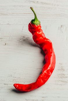 One red chili pepper over light wooden background.