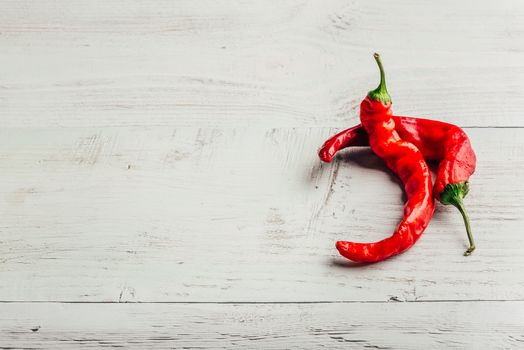 Ripe and red chili peppers over light wooden background.