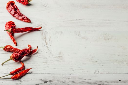 Dried red chili peppers over light wooden background