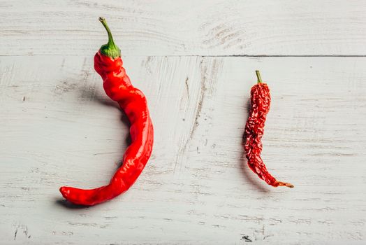 Two red chili peppers, fresh and dry, over wooden background