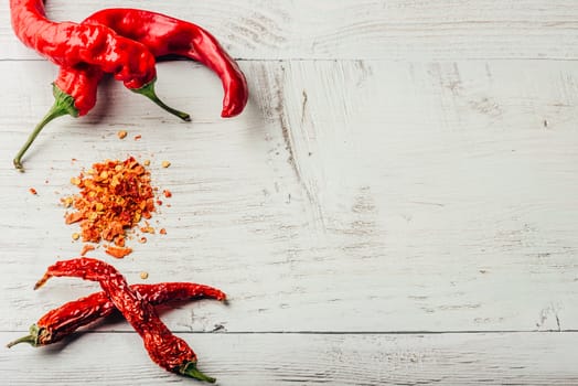 Fresh, dried and crushed red chili pepper over white wooden background.