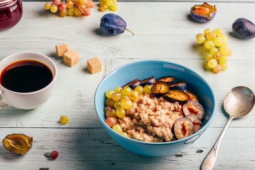 Healthy breakfast concept. Porridge with fresh plum, green grapes and cup of coffee. Ingredients over wooden background.