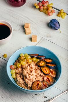 Healthy breakfast concept. Porridge with fresh plum, green grapes and cup of coffee.