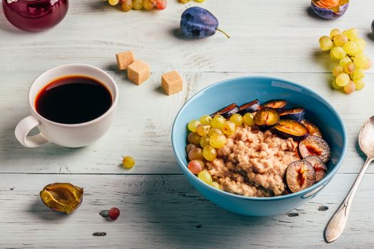 Healthy breakfast concept. Porridge with fresh plum, green grapes and cup of coffee.