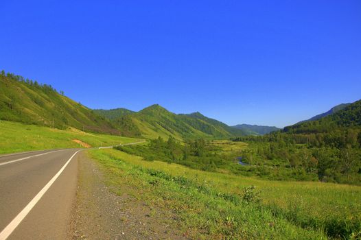 Asphalt road going through a fertile valley surrounded by a choir. Altai, Siberia, Russia.