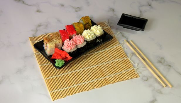 Sushi set with red ginger and wasabi on a bamboo napkin, bowl with soy sauce and chopsticks.