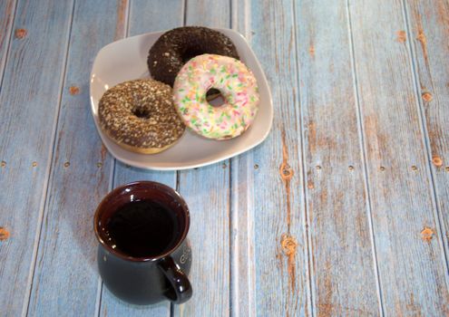 Three donuts in the icing on the plate and a cup of tea on the wooden table.